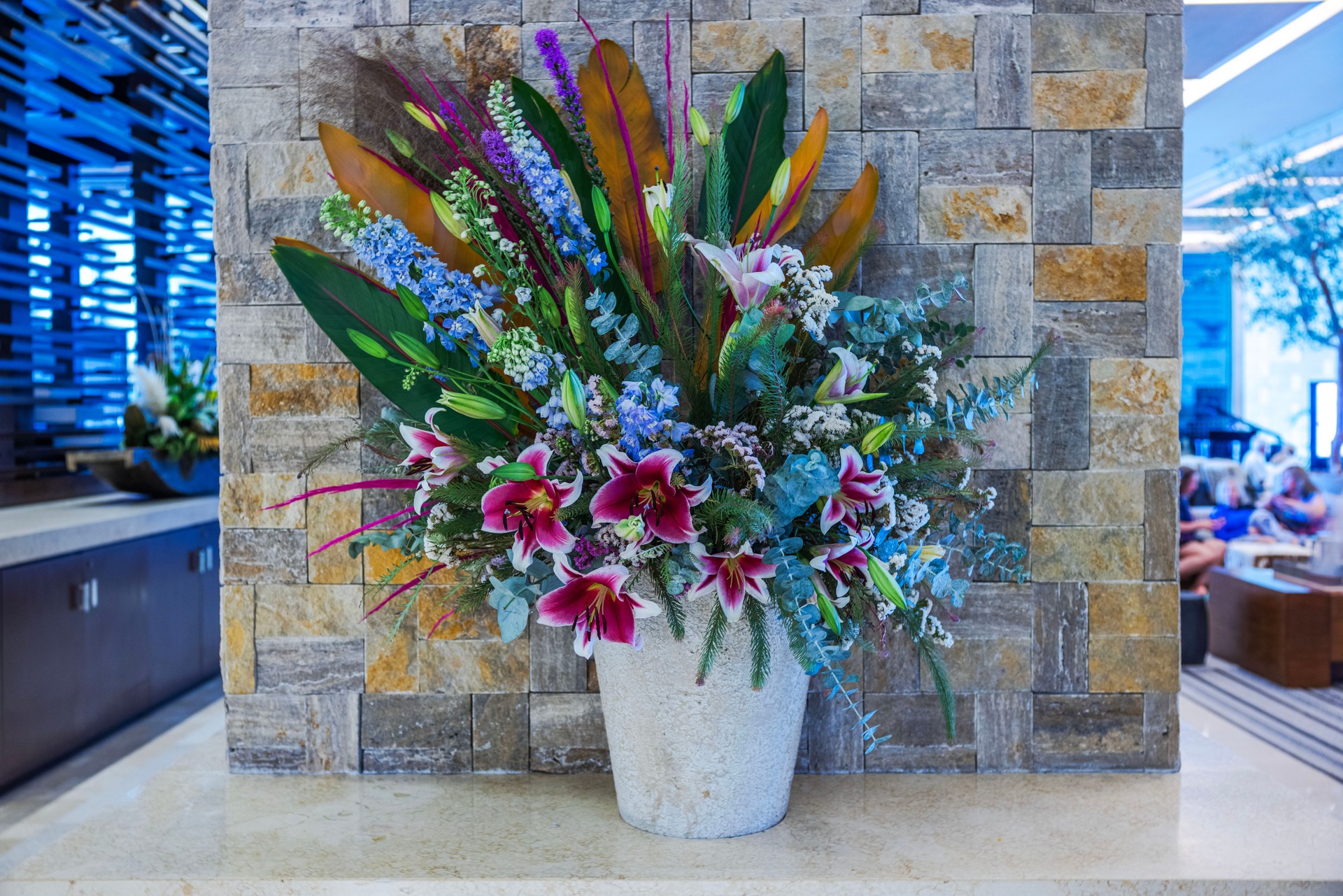 Elegant floral arrangement with pink lilies and blue flowers in stone vase against decorative stone wall in hotel lobby. Mexico. Cancun.